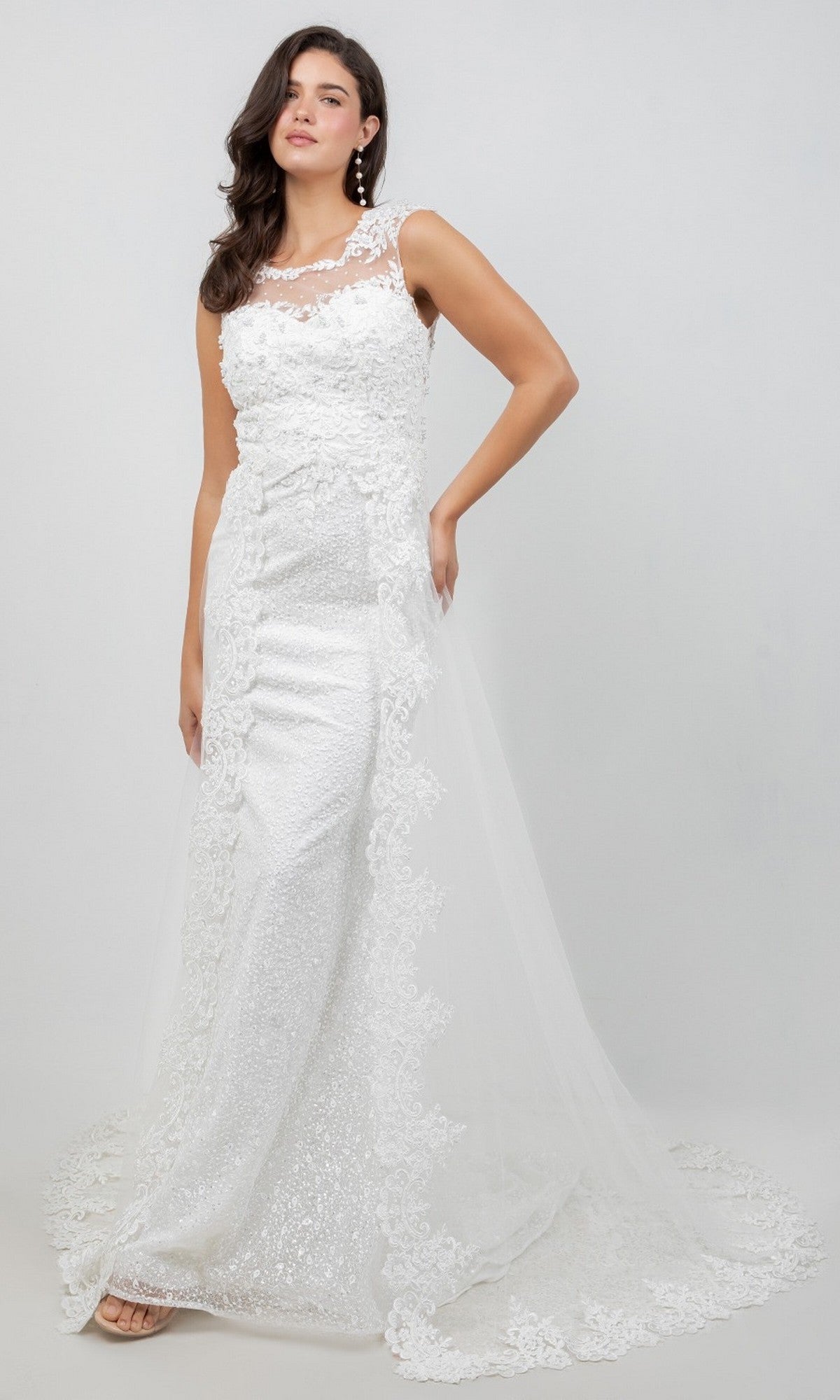 A woman poses in the Cinderella Couture 8506J long formal dress, featuring an off-white floor-length design with a sheer tulle overlay, intricate lace appliqués, floral detailing, and a small train, set against a plain light background.